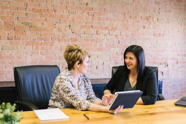 Two business women talking while one has an open laptop