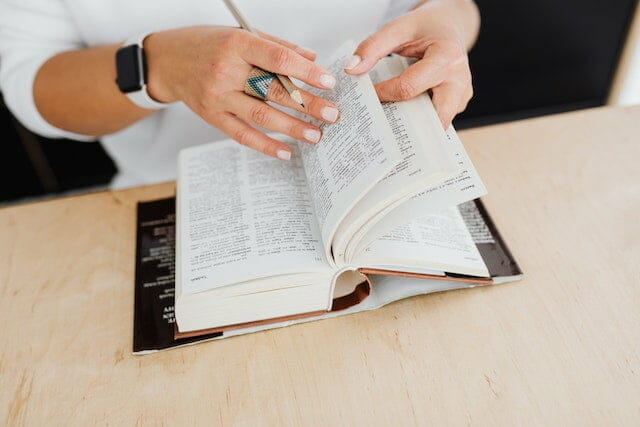 A woman turning pages in a dictionary translating from a foreign language.